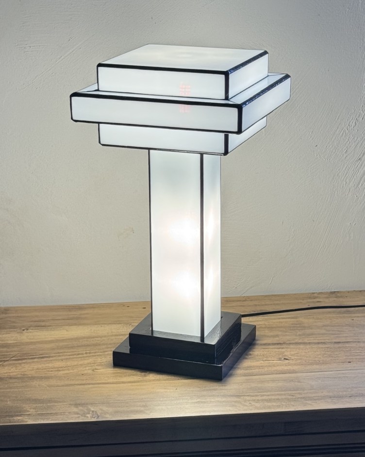 Lampe design rectangulaire en verre dépoli et métal noir, posée sur une table en bois, diffusant une lumière douce et moderne