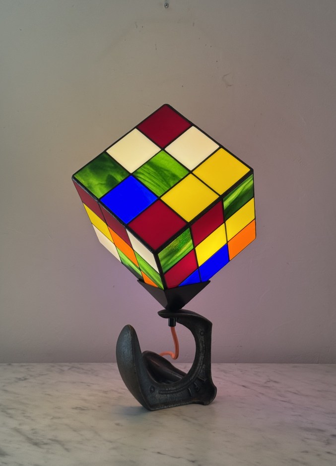 Lampe originale en forme de Rubik's Cube coloré montée sur un socle en métal, posée sur une table en marbre